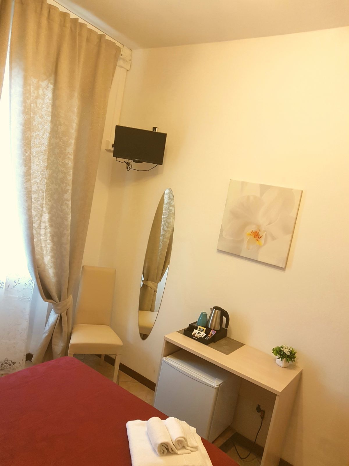 Une chambre d’hôtel avec un lit, un bureau avec un ordinateur, un miroir, une petite plante et un tableau au mur.