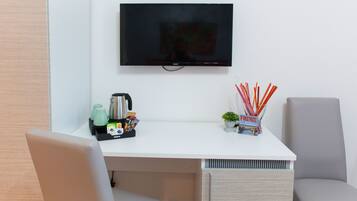 A modern room with a white desk, a flat-screen TV mounted on the wall, a coffee maker, a small plant, and a magazine.