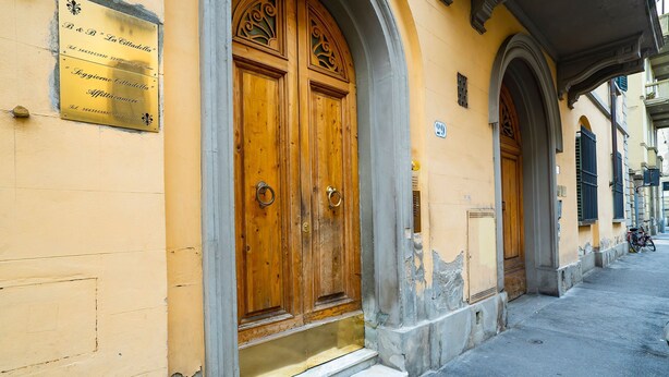 Um edifício com uma grande porta dupla de madeira, uma placa acima da porta e um pequeno degrau que leva à entrada.