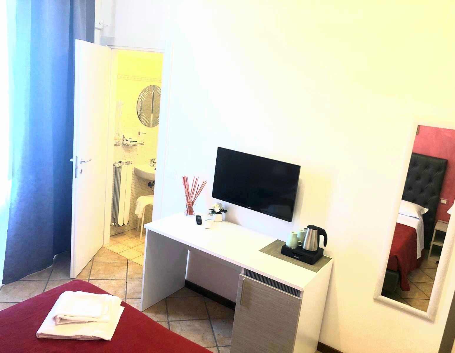 Habitación de hotel con cama, escritorio con televisor, espejo y baño a la vista a través de una puerta abierta.