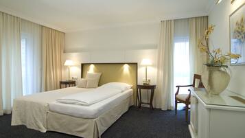 Ein Hotelzimmer mit einem großen Bett, zwei Nachttischen mit Lampen, einem Sessel, einem Schreibtisch und einer Vase mit Blumen.