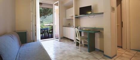Una habitación pequeña con cama, escritorio, silla y televisor.