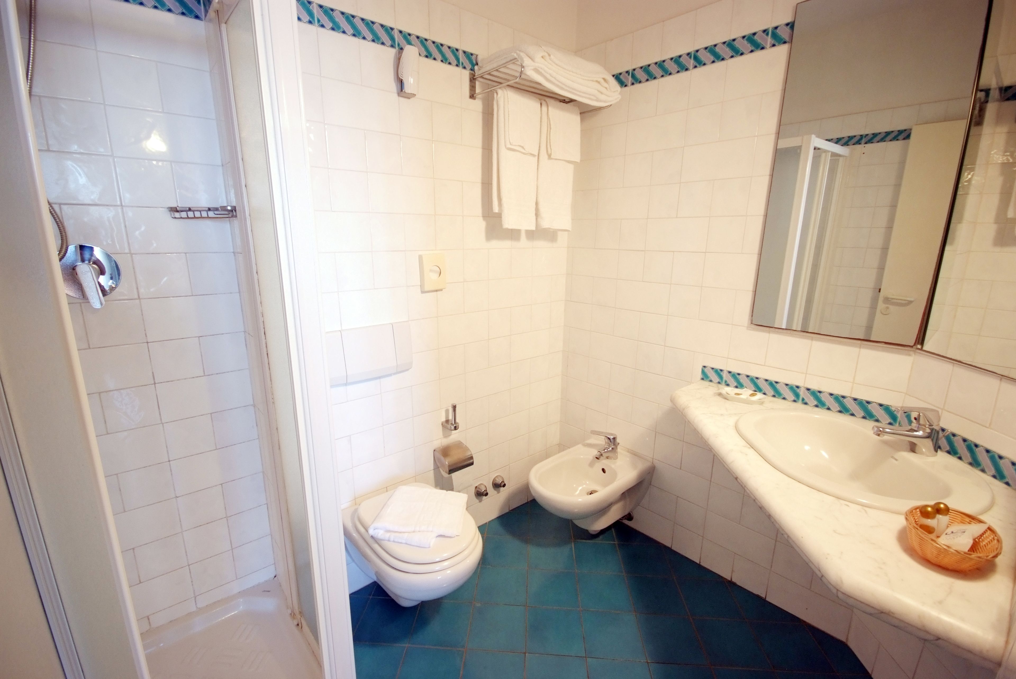 A bathroom with a toilet, bidet, and sink, with blue and white tiles and a mirror above the sink.