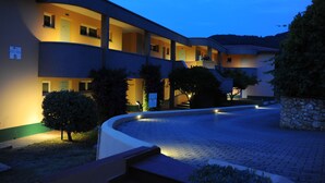 A multi-story hotel with a curved facade, outdoor lighting, and a paved courtyard. - Isola Verde (Marciana Marina)