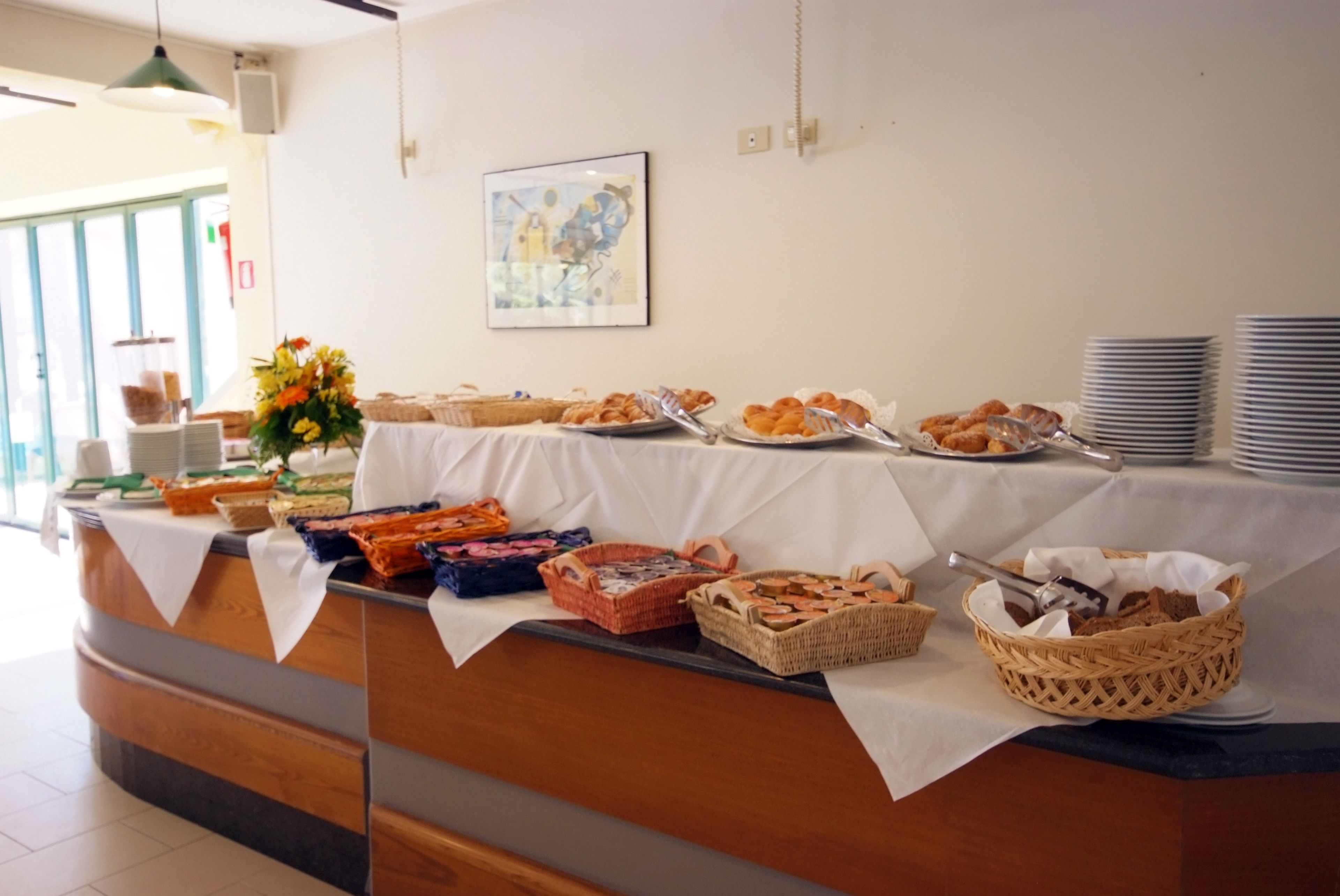 Un buffet est installé sur une table, avec divers plats et des paniers. Un tableau orne le mur et une fenêtre se trouve à l’arrière-plan.