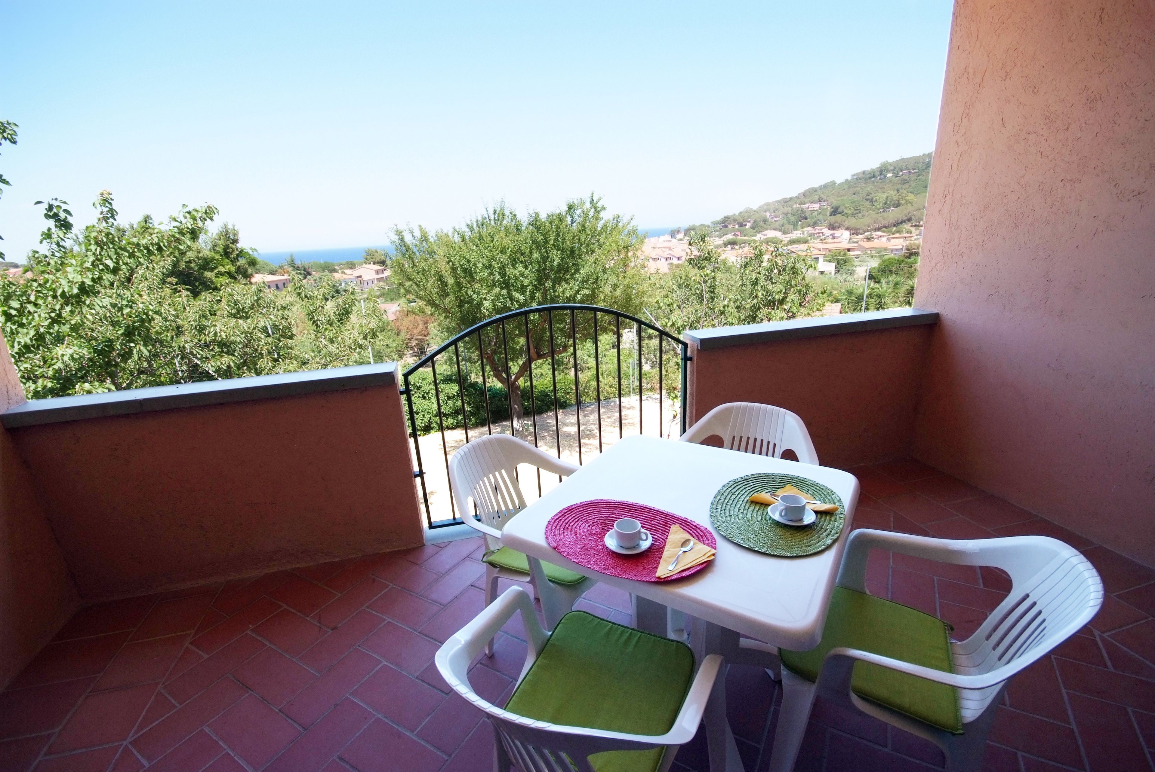 A balcony with a table set for two, chairs, and a view of a coastal landscape.