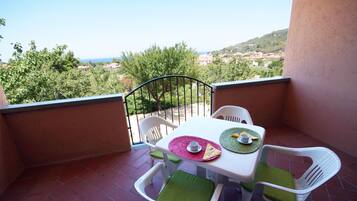A balcony with a table set for two, chairs, and a view of a coastal landscape.