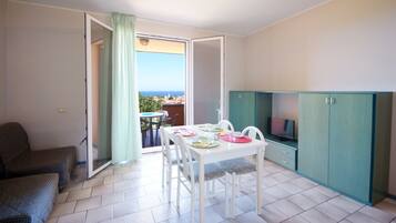 Una stanza con un tavolo da pranzo per quattro persone, un divano, una TV e vista mare.