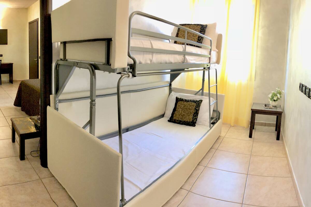 A bunk bed with a desk and chair, a small table with a vase, and a TV in a room with tiled floors.