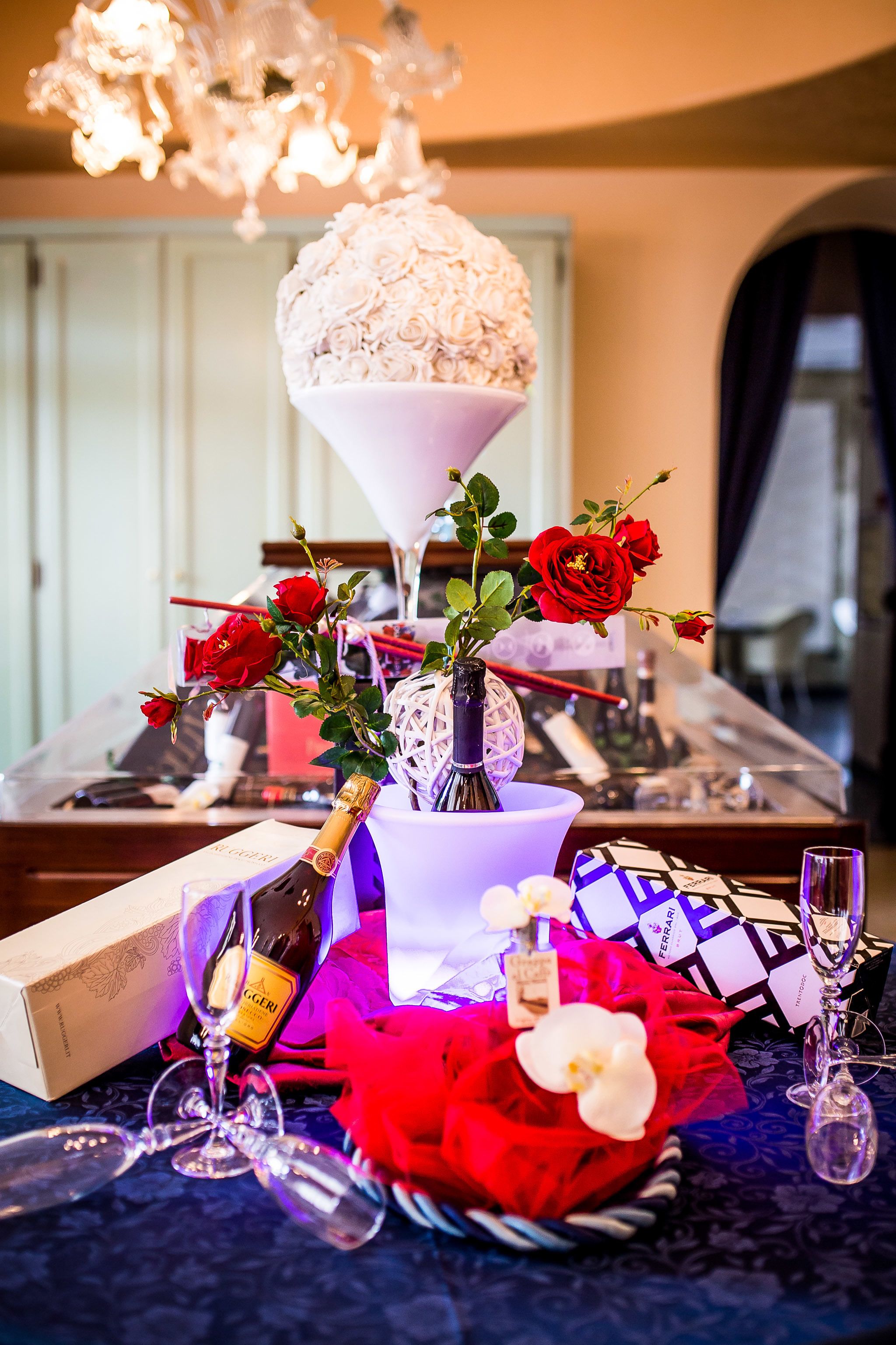 A dining table with a bottle of champagne, a vase with red roses, and a decorative glass arrangement.
