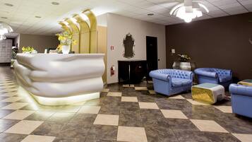 Un'area reception di un hotel dal design moderno, con una reception originale, divani blu e un pavimento a scacchi.