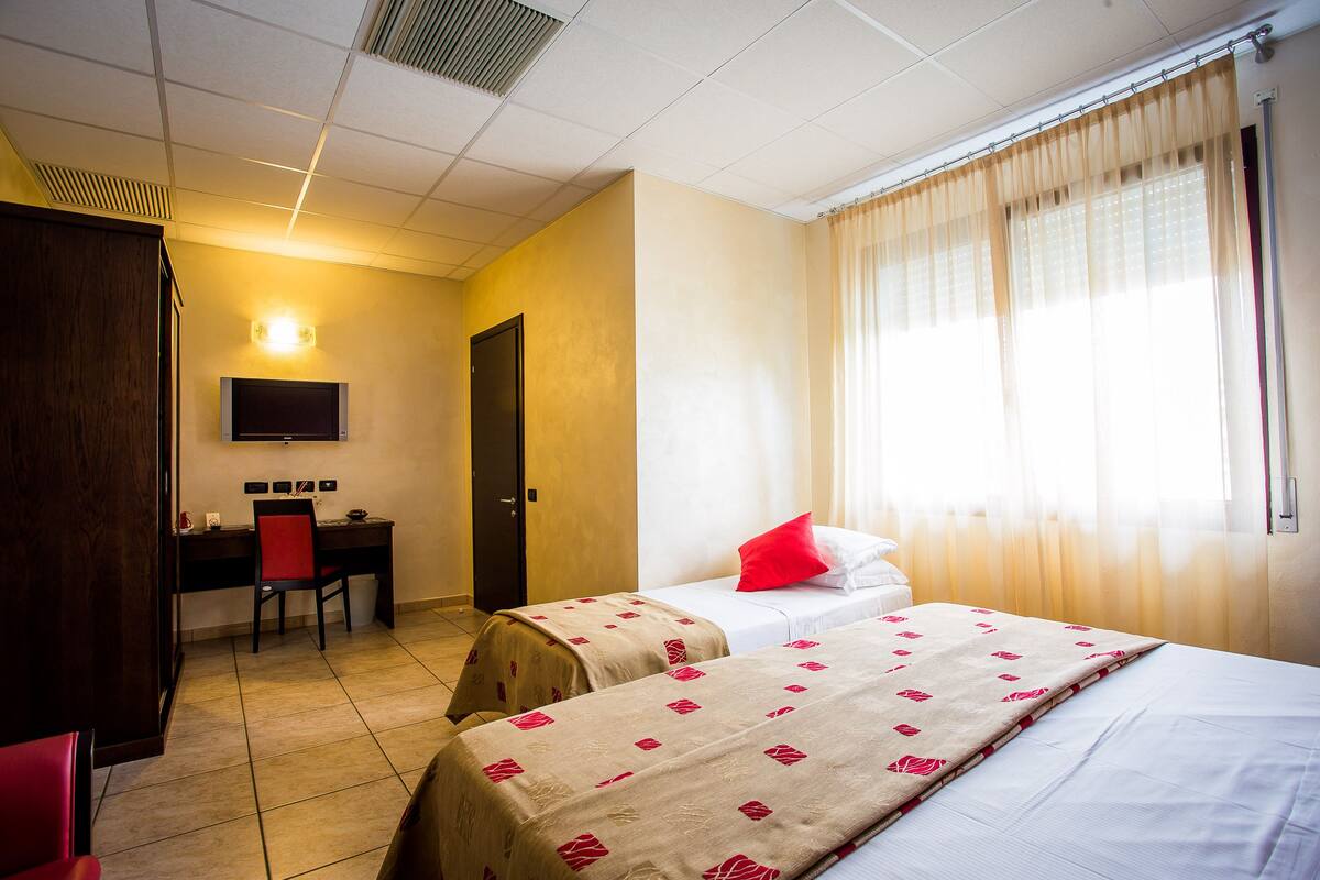 A hotel room with two beds, a desk with a chair, a TV, and a window with curtains.