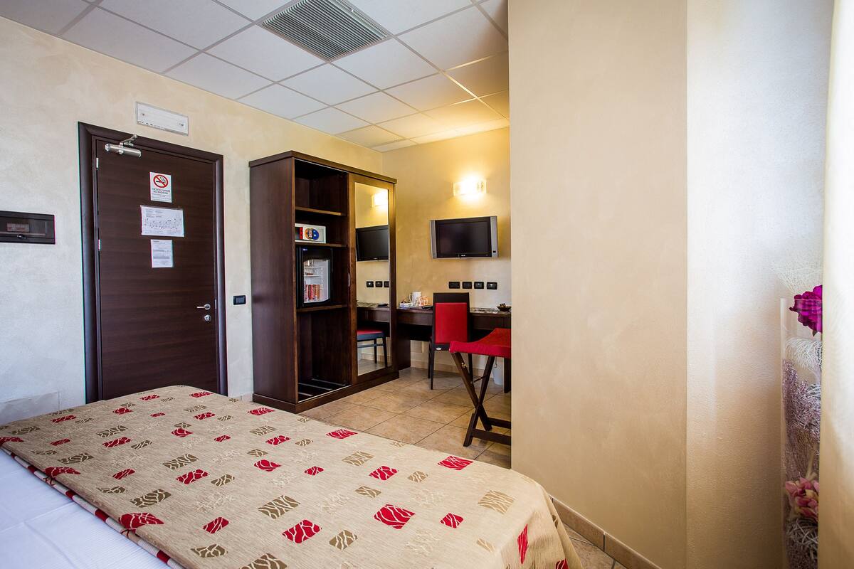 A hotel room with a bed, a desk, a chair, a TV, and a wardrobe.
