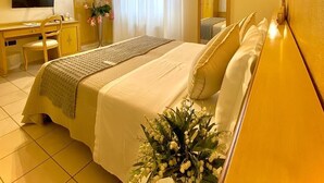 Una habitación de hotel con cama, escritorio, silla, televisor y espejo.