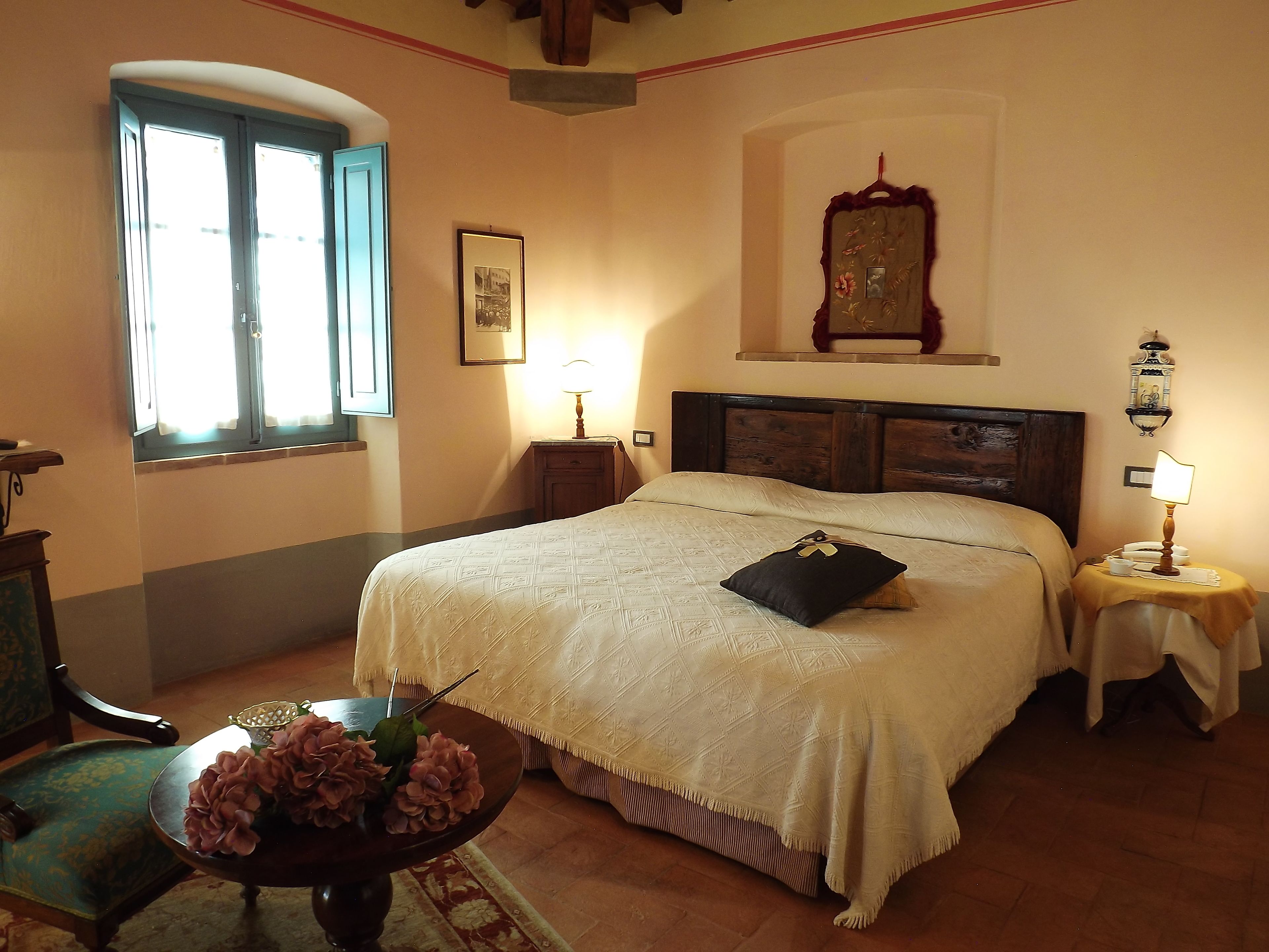 Un dormitorio con una cama grande, una mesita de noche con lámpara, una ventana y un cuadro en la pared.