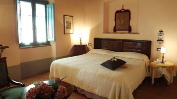 Un dormitorio con una cama grande, una mesita de noche con lámpara, una ventana y un cuadro en la pared.