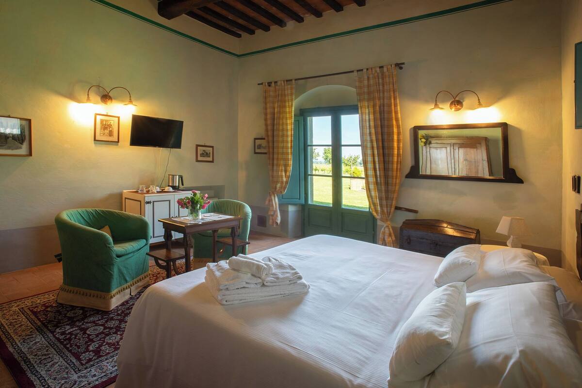 Habitación de hotel con cama, escritorio con computadora, silla y ventana con cortinas.
