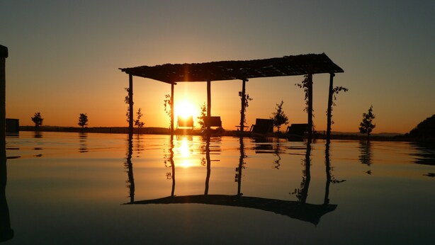 A tranquil sunset over a calm body of water with a gazebo structure in the foreground. - Cortona Resort - Le Terre Dei Cavalieri (Cortona)