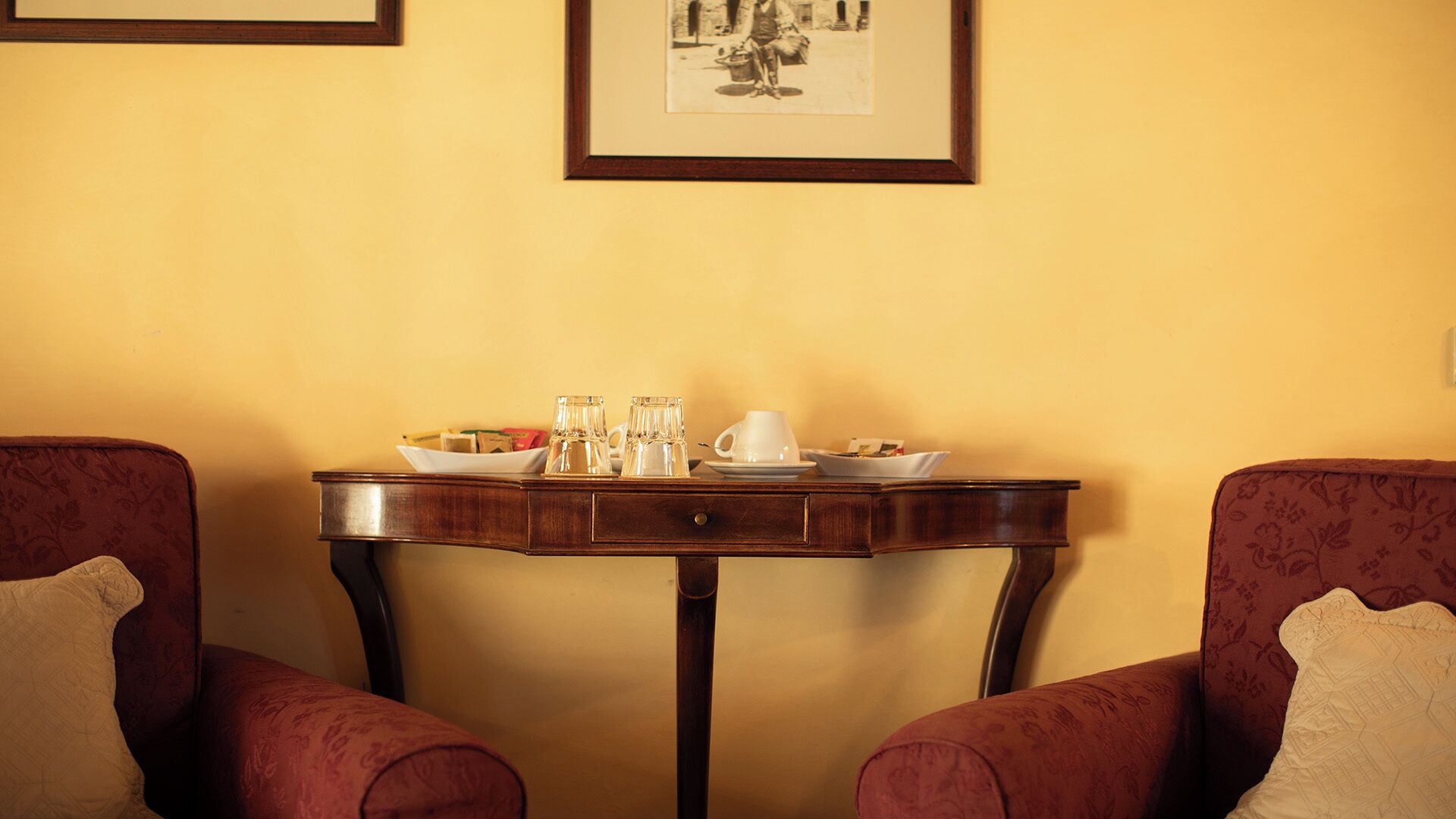Una habitación con una mesa de madera dispuesta para el desayuno, dos sillones y un cuadro en la pared.