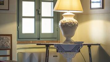 Ein Zimmer mit einer Tischlampe, einem Fenster mit grünem Rahmen und einem kleinen Tisch mit weißer Spitzenleinentuch.