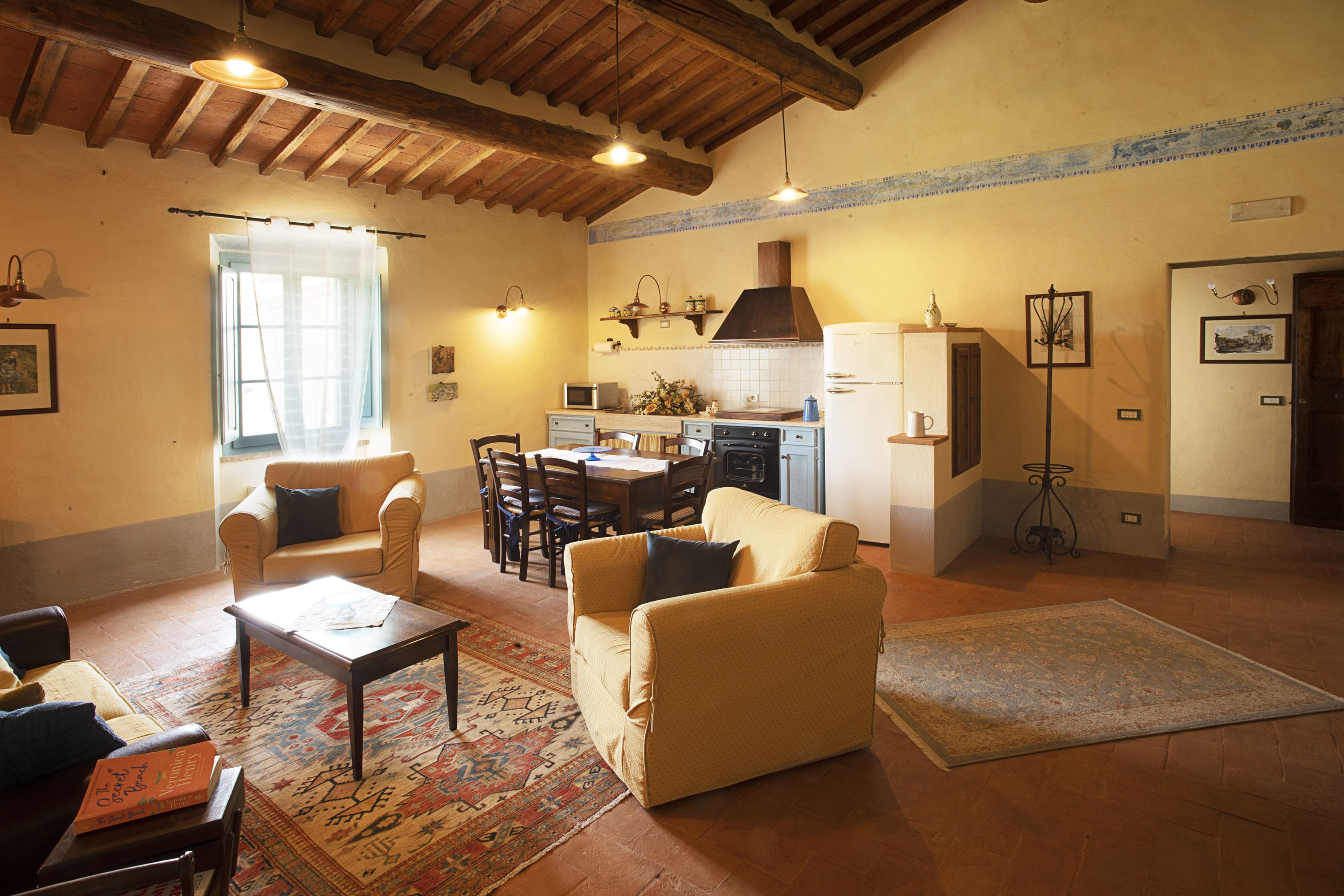 Una sala de estar acogedora con sofá, mesa de centro y alfombra. Hay un comedor con sillas y mesa, y una cocina con estufa y refrigerador.