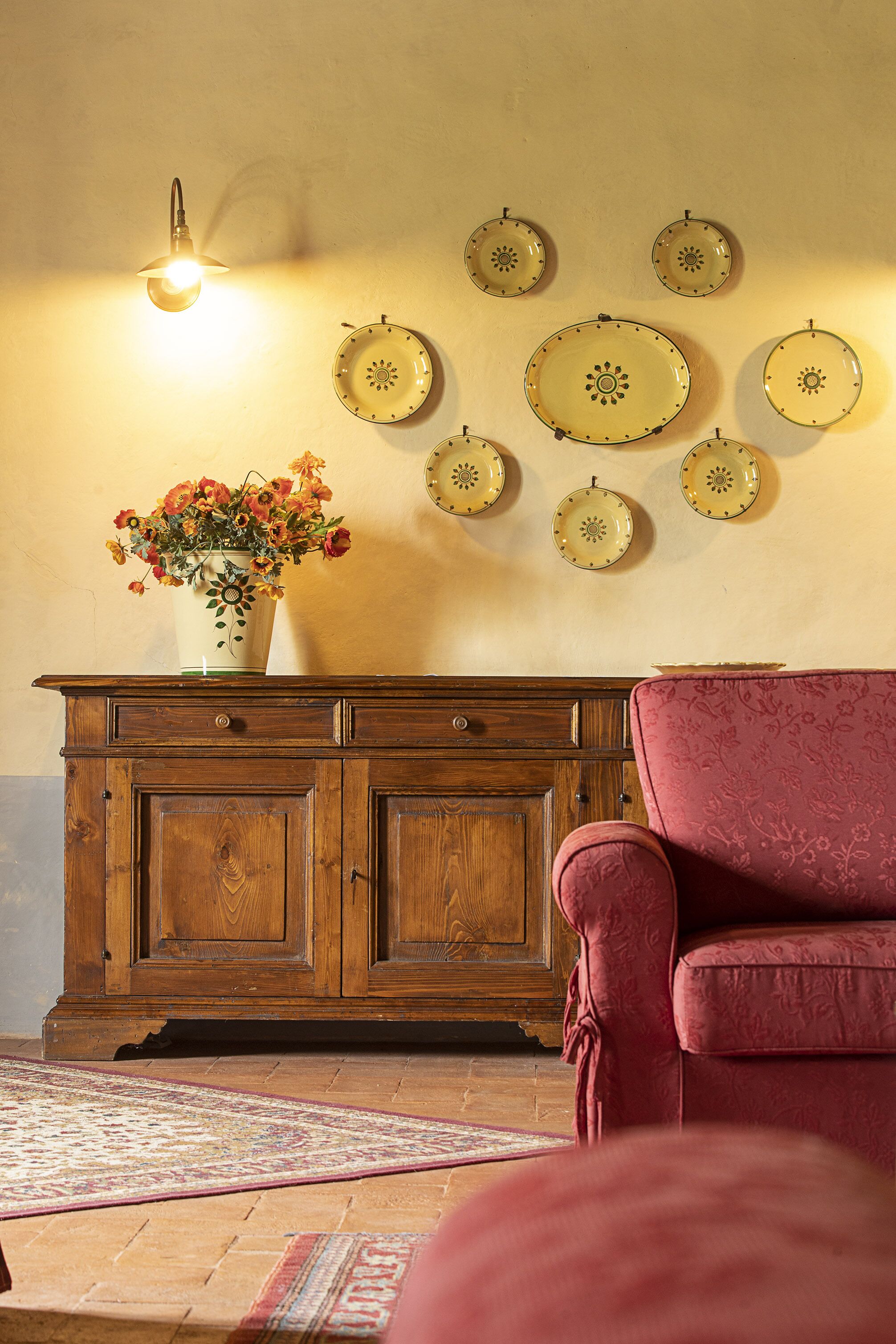 A wooden cabinet with a vase of flowers, a pink chair, and wall-mounted plates.