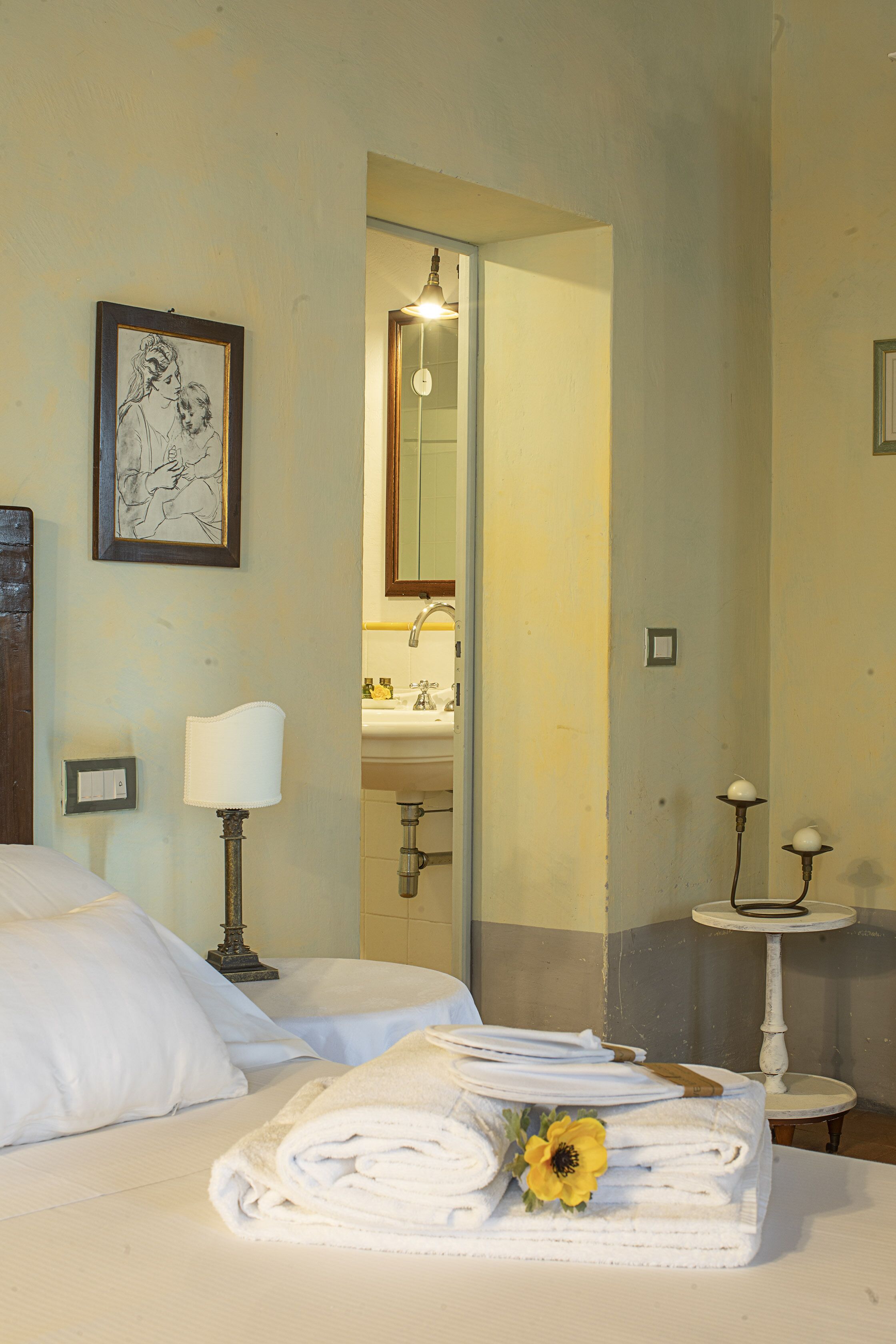 A hotel room with a bed, a bedside lamp, a framed picture on the wall, and a bathroom visible through an open door.