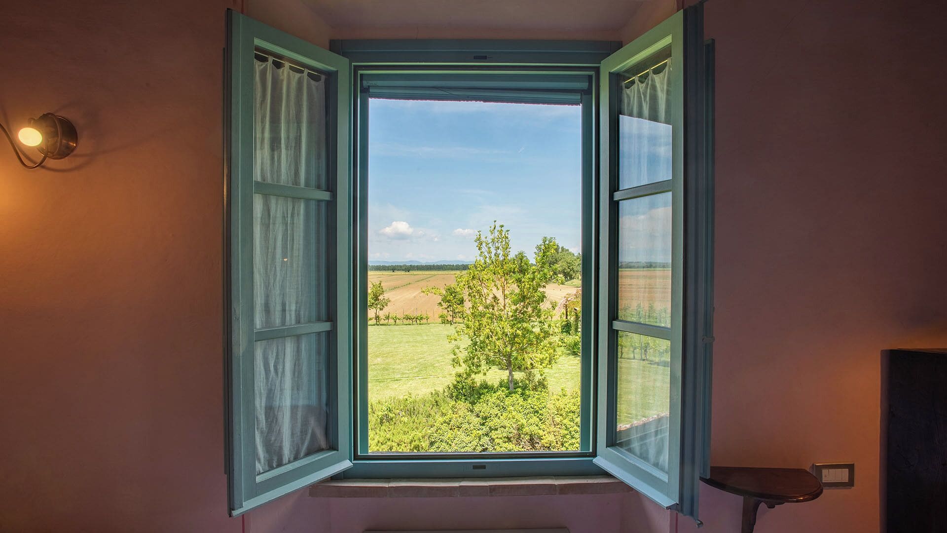 Une fenêtre ouverte donnant sur un paysage verdoyant et un ciel dégagé.