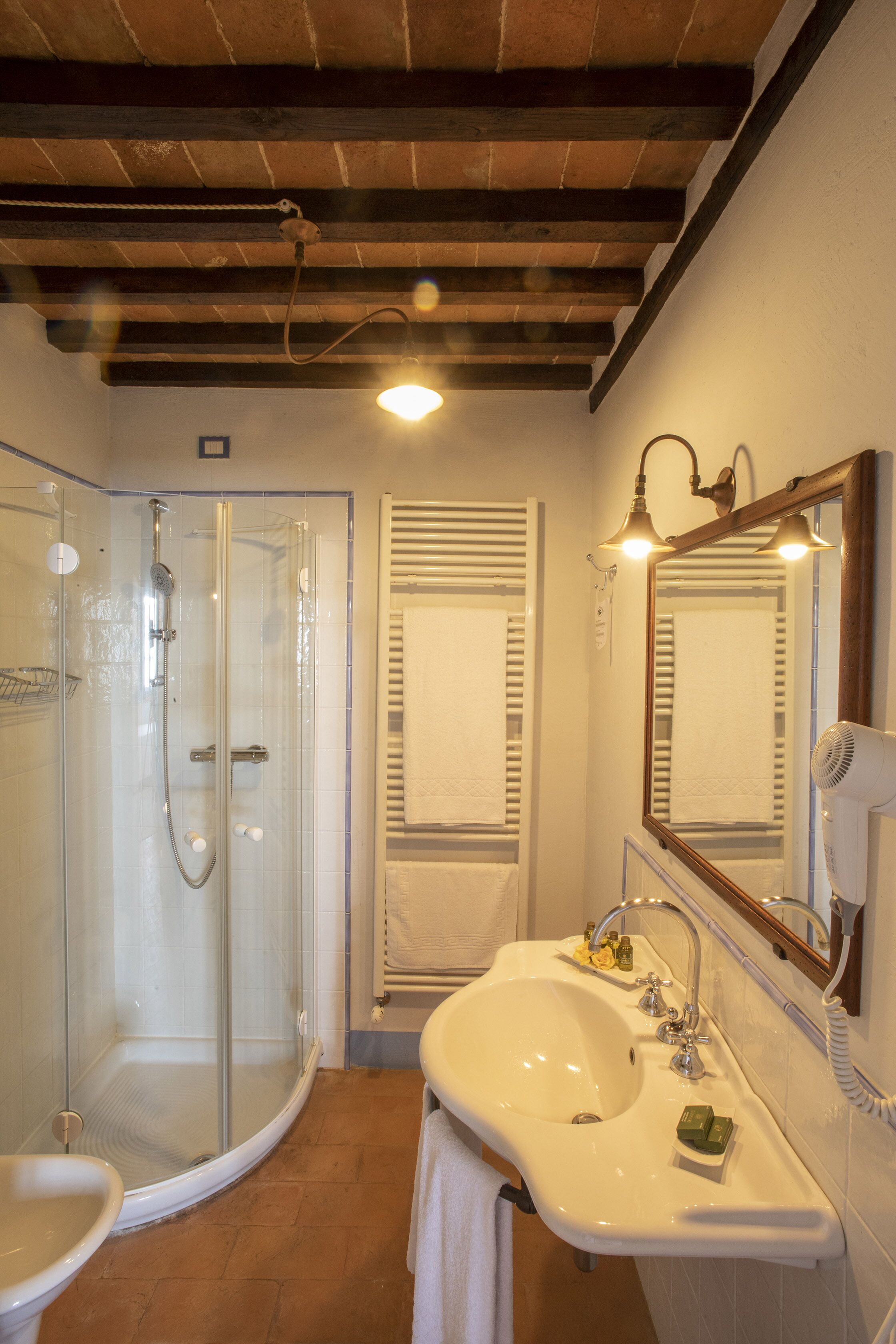 Casa de banho com cabine de chuveiro em vidro, pia branca com espelho e porta-toalhas.