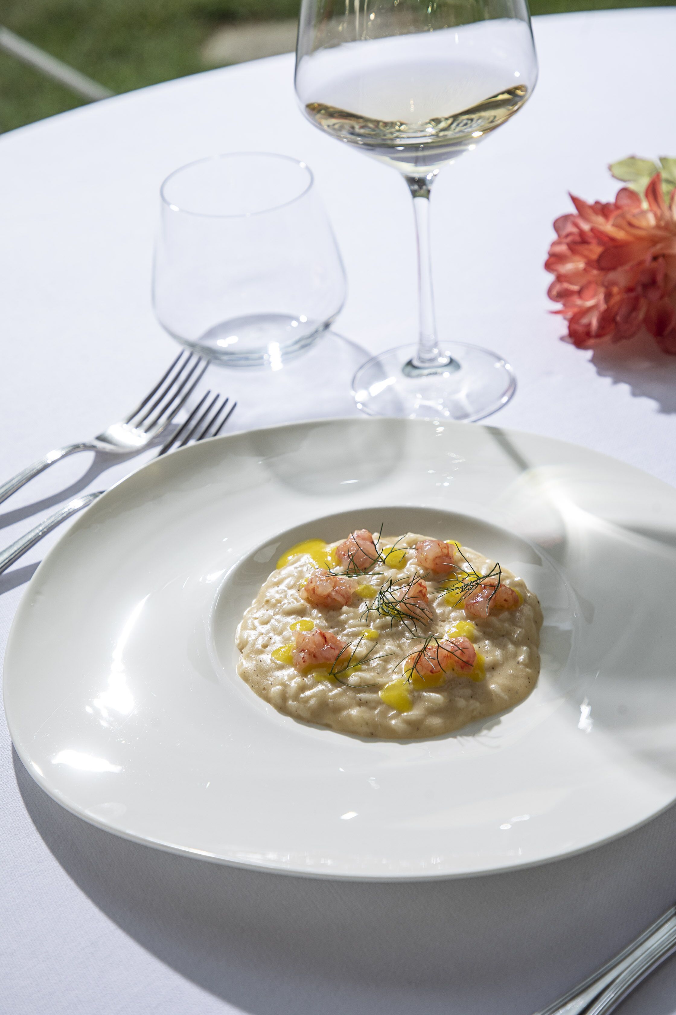Une assiette blanche contenant un plat de fruits de mer, un verre à vin et une fourchette, le tout posé sur une nappe blanche.