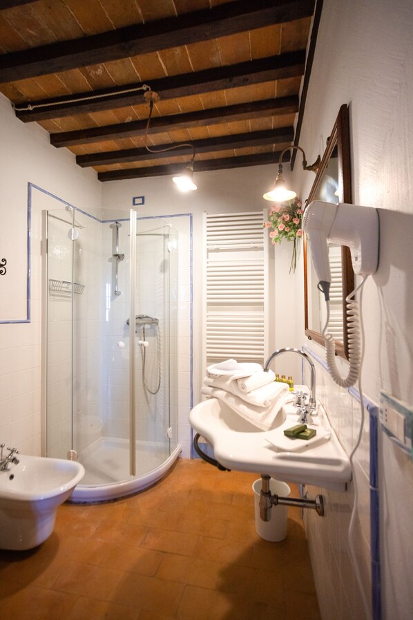 A bathroom with a glass-enclosed shower, a sink with a mirror, and a hairdryer mounted on the wall. - Cortona Resort - Le Terre Dei Cavalieri (Cortona)
