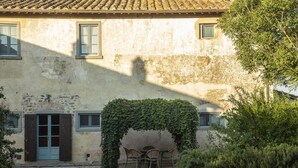 A building with a rustic facade, a door with shutters, and a small outdoor seating area under a vine-covered archway. - Cortona Resort - Le Terre Dei Cavalieri (Cortona)