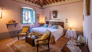 A cozy bedroom with a large bed, two armchairs, a small table with a teapot, and a window with a view of trees. - Cortona Resort - Le Terre Dei Cavalieri (Cortona)