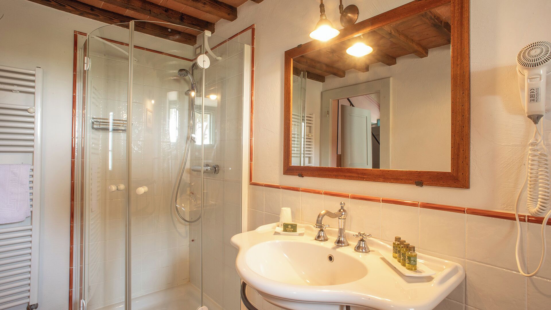 A bathroom with a glass-enclosed shower, a white sink with a mirror above it, and a hairdryer mounted on the wall.