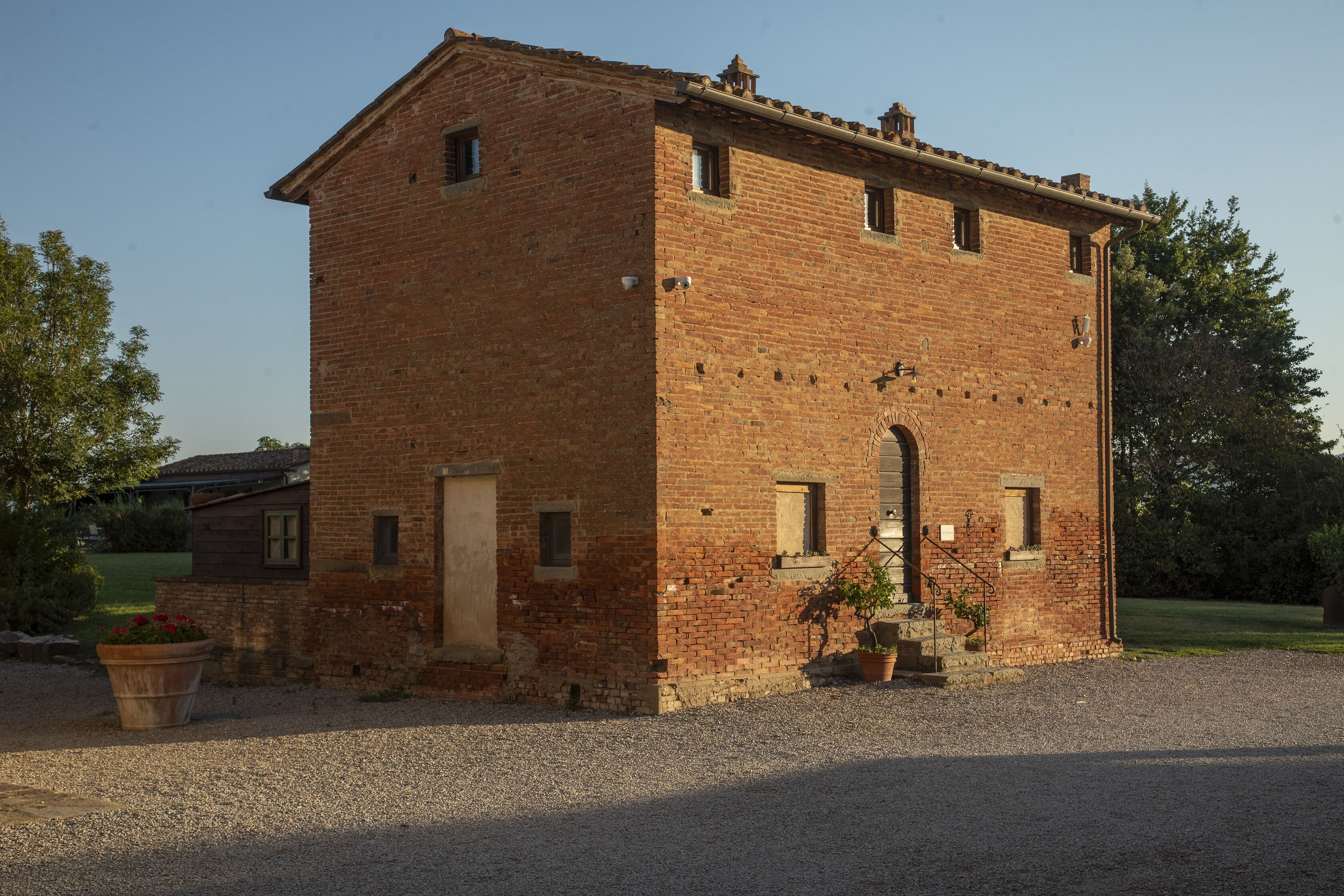 Un bâtiment à deux étages, construit en briques, avec une entrée centrale, des fenêtres et un petit porche agrémenté de plantes en pot.