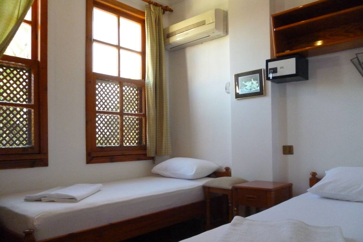 A room with two single beds, a small wooden table, a wall-mounted TV, and a window with a lattice design.