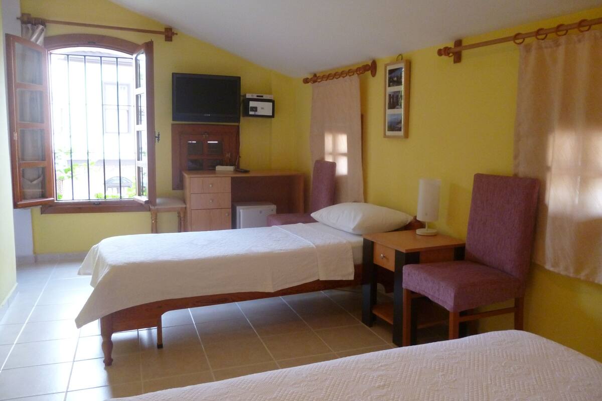 A room with two beds, a desk, a chair, a television, and a window with curtains.