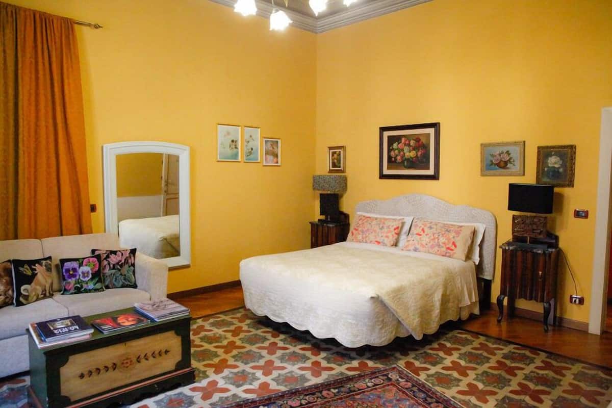Un dormitorio con cama, sofá, espejo y una pequeña mesa.