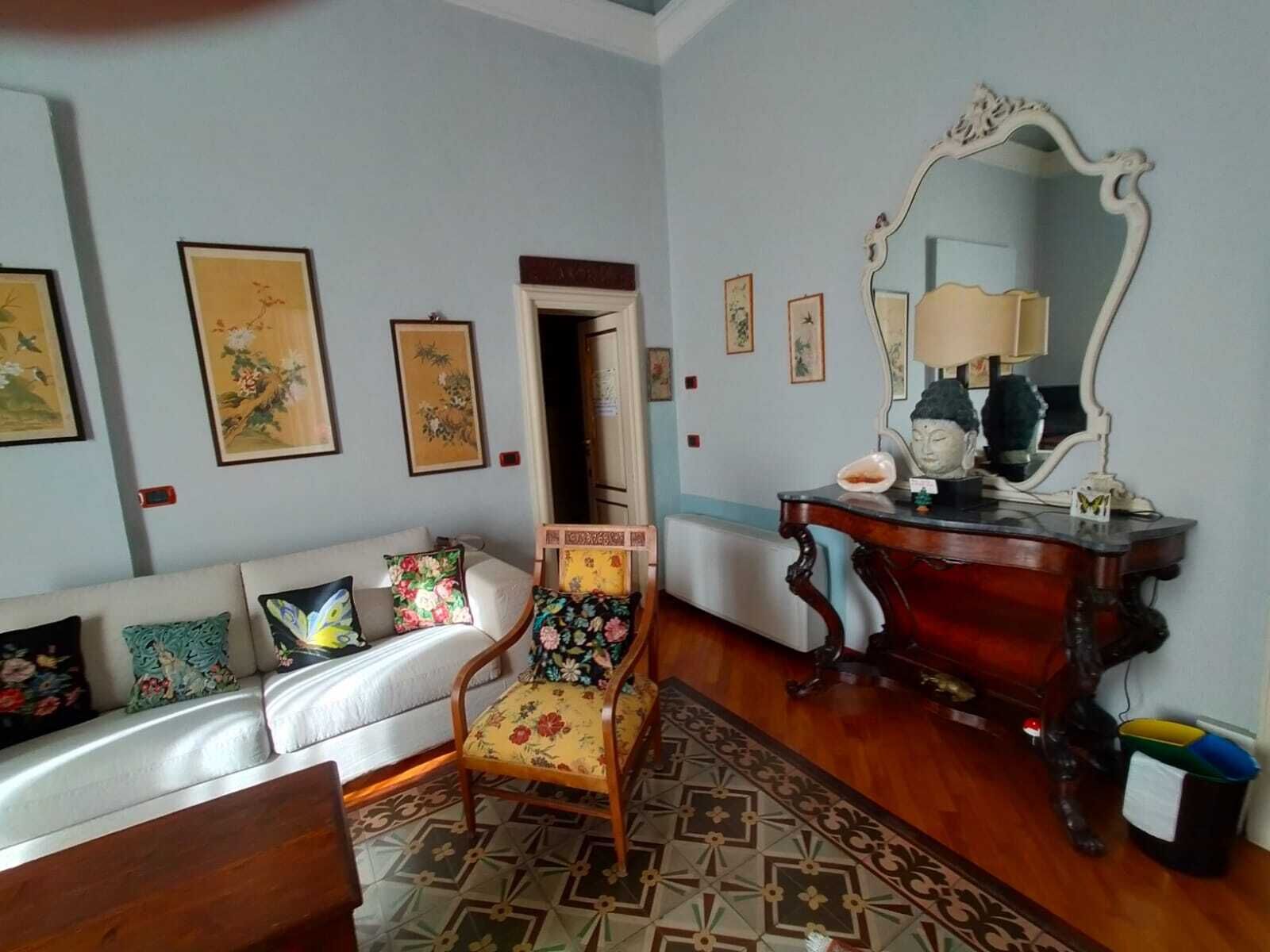 Ein Zimmer mit einer Couch, einem Sessel, einem Holztisch und einem Spiegel. An der Wand befinden sich Bilder in Rahmen.
