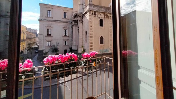 A balcony with pink flowers and a view of a historic building with a tower. - B&B Crociferi Catania (Catania)
