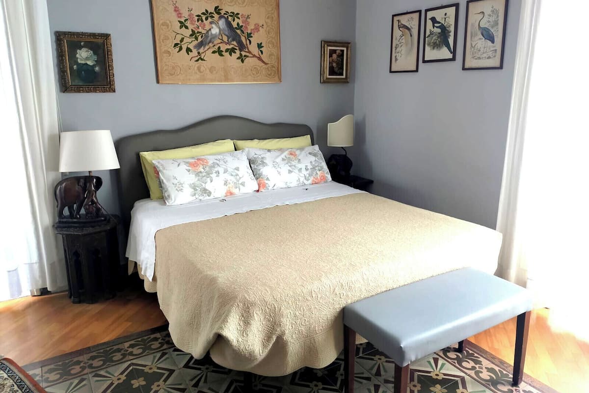 Un dormitorio ordenado con cama, mesitas de noche, un banco y obras de arte enmarcadas en las paredes.