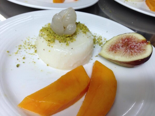 Een dessertborden met een witte, romige topping gegarneerd met groen, vergezeld van een gehalveerde vijg en twee oranjeslices.