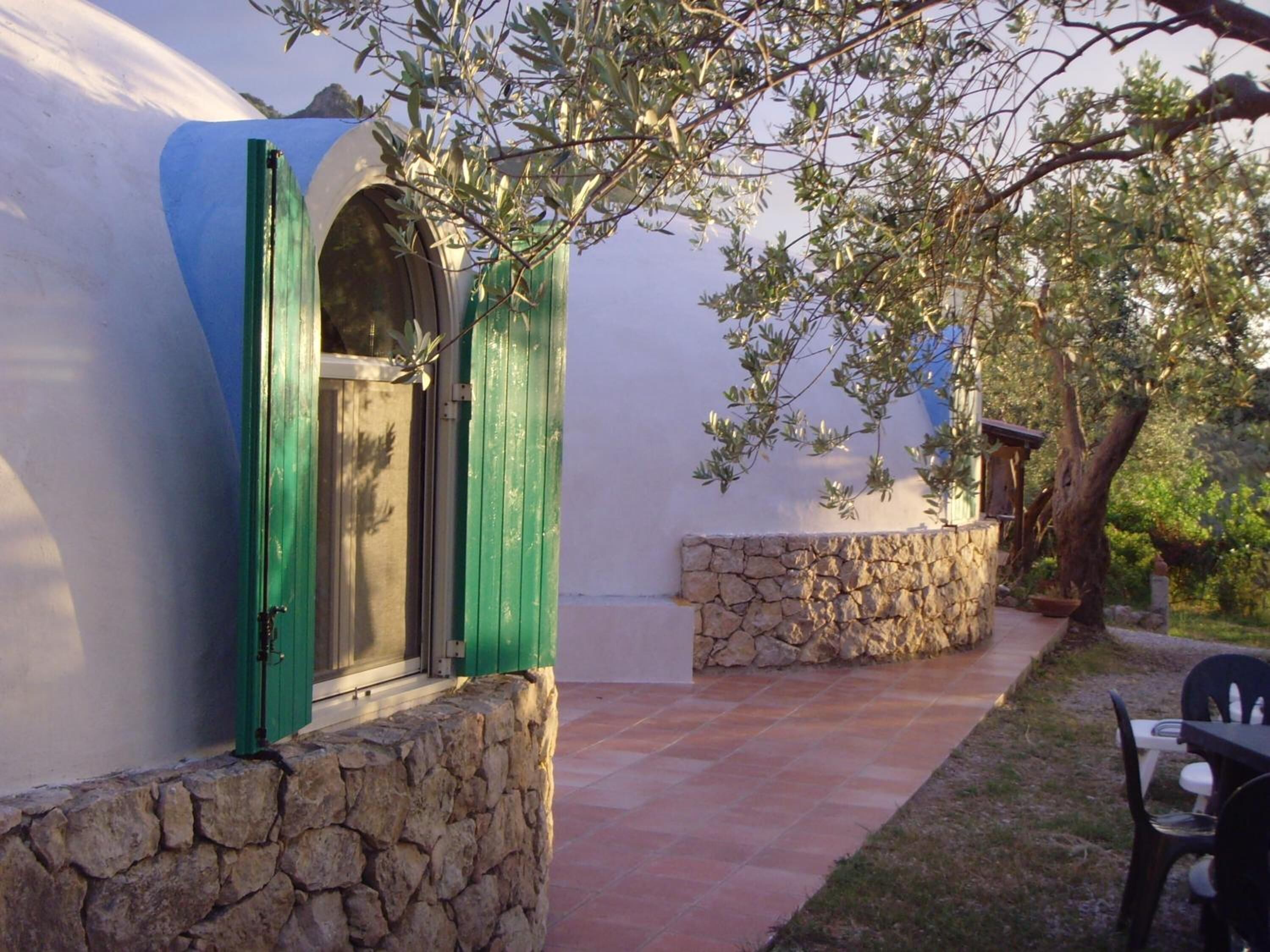 A stone wall with a window and a door, a stone pathway, and a tree.