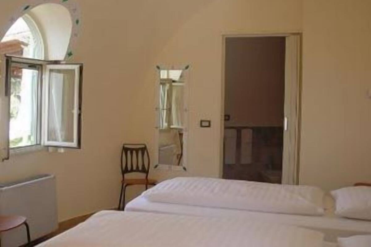 Une chambre à coucher avec un lit, une chaise, un radiateur et une fenêtre dont le volet est ouvert.