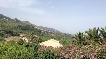 Un paisaje montañoso con edificios dispersos, abundante vegetación y una colina destacada al fondo.