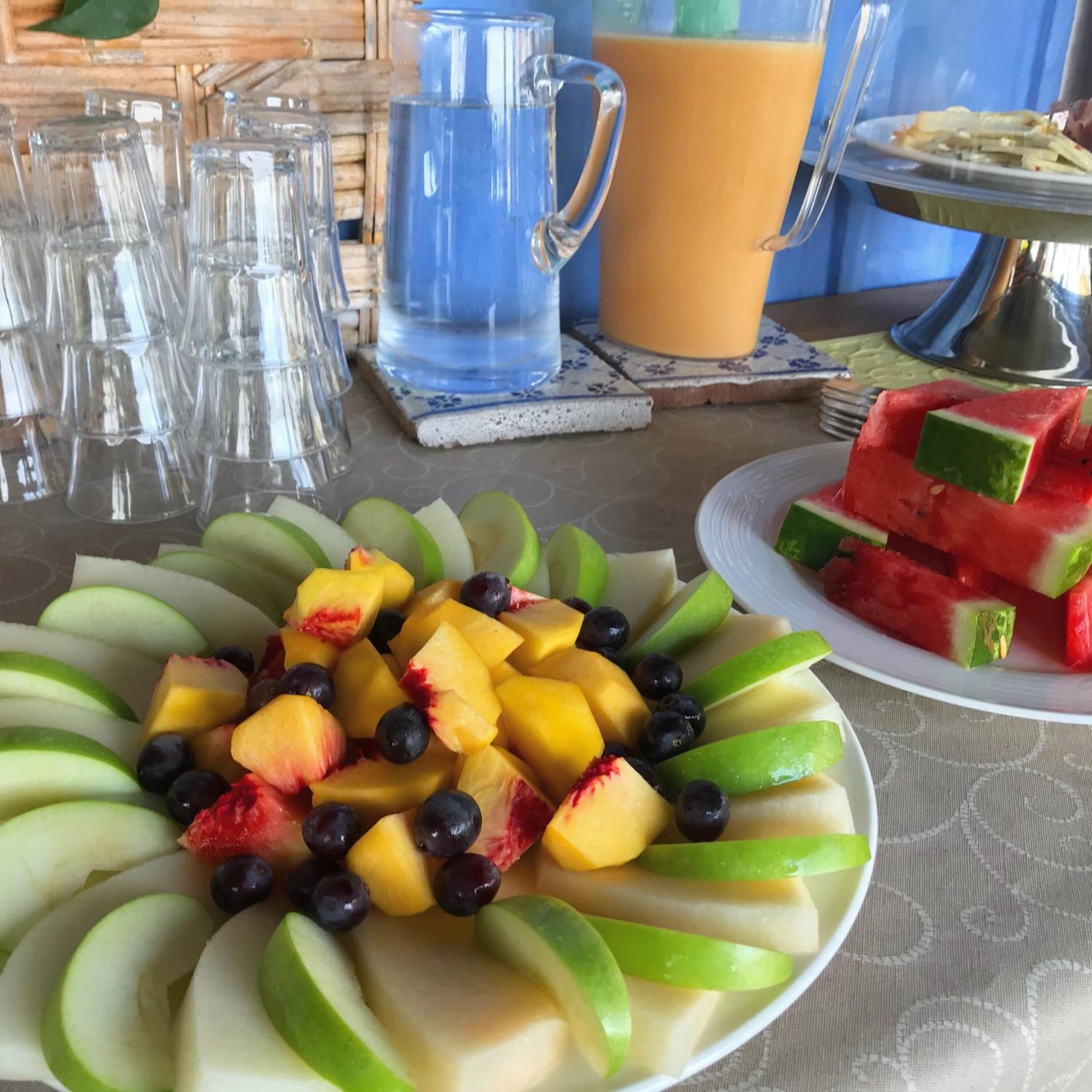 A table with a fruit platter, a pitcher of water, and a cup of coffee.