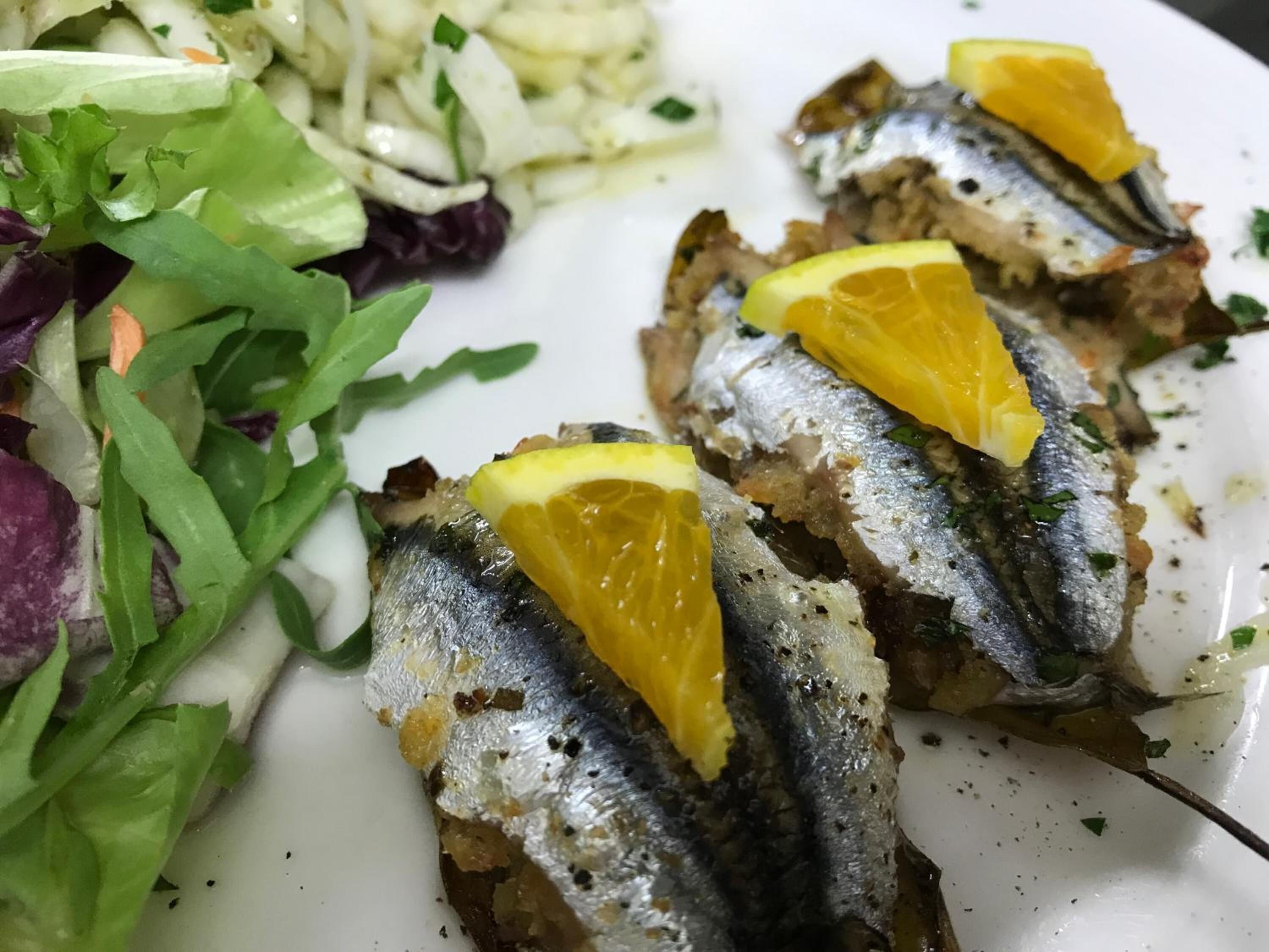 Ein Teller gegrillter Sardinen mit Zitronenscheiben, dazu ein gemischter Salat.