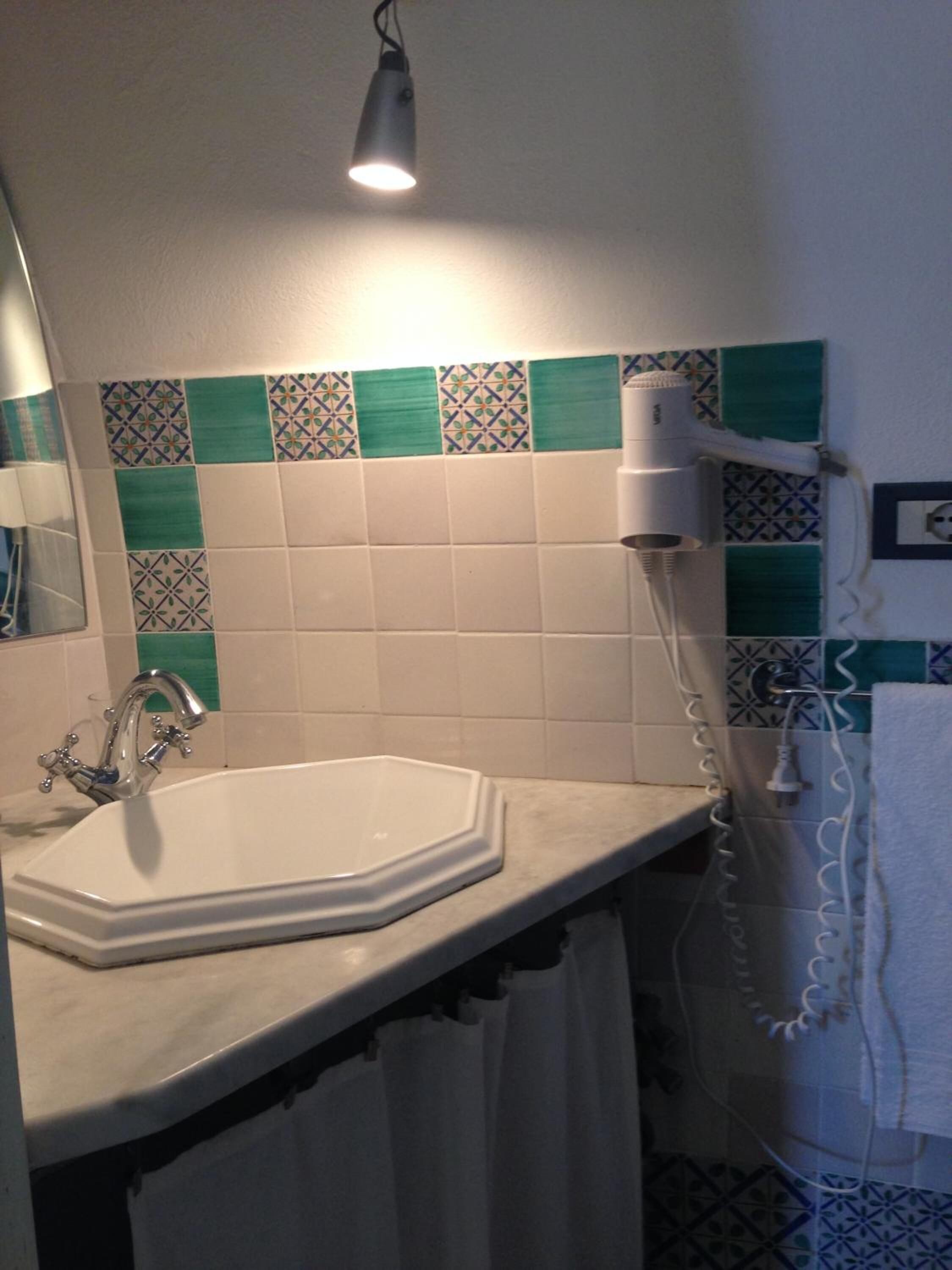 Une salle de bain avec un lavabo blanc, un miroir, un porte-serviettes et un sèche-cheveux.