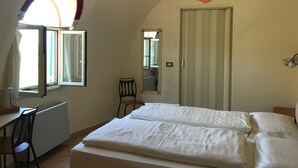 Un dormitorio con cama, escritorio, silla, mesita, espejo y armario.