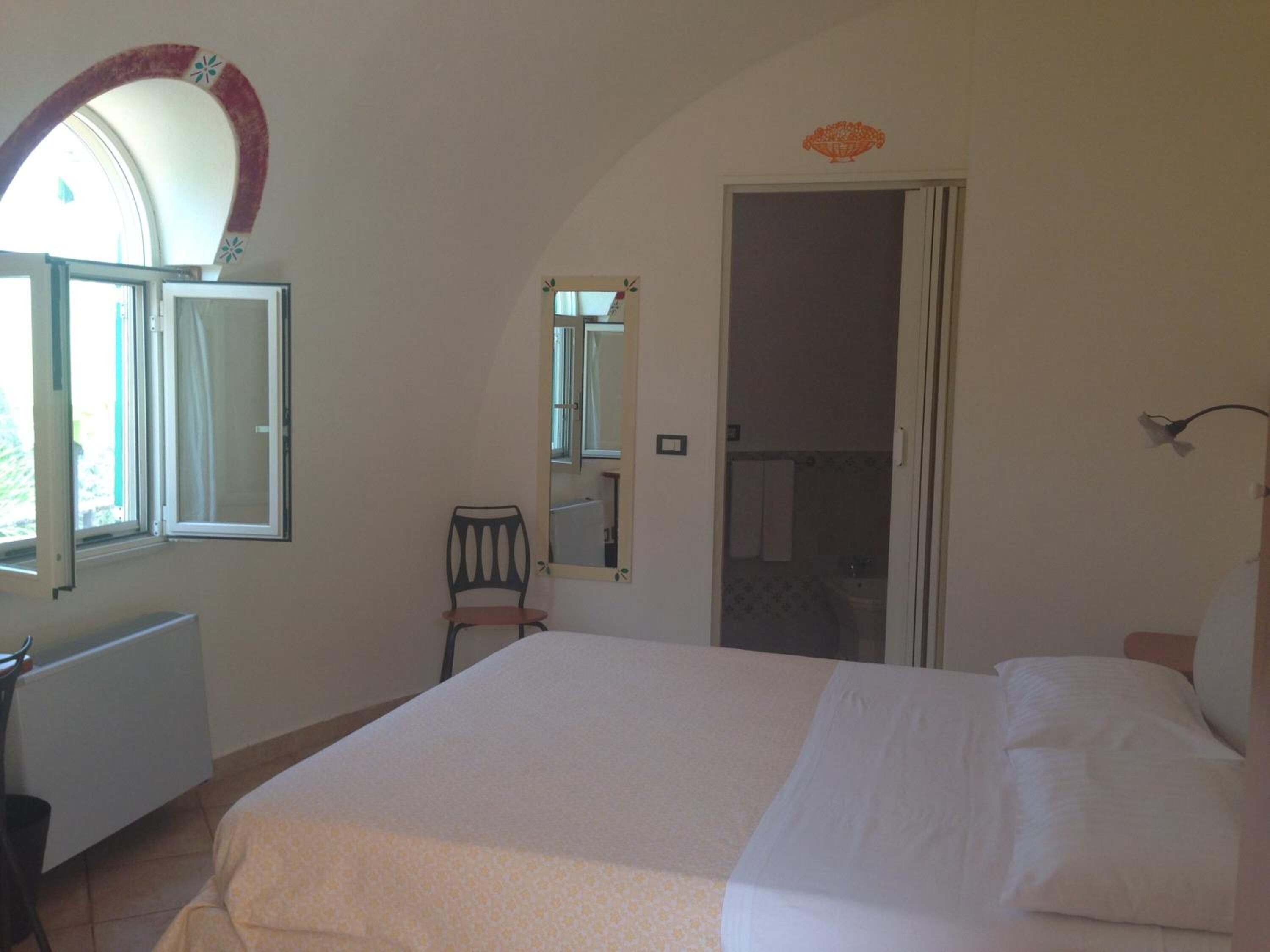 A bedroom with a bed, a chair, a radiator, a window, and a mirror.